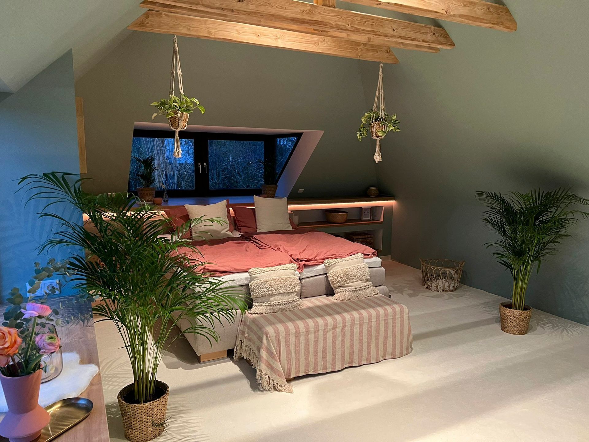 ein Schlafzimmer mit einem Bett, Pflanzen, einer Bank und einem Fenster.