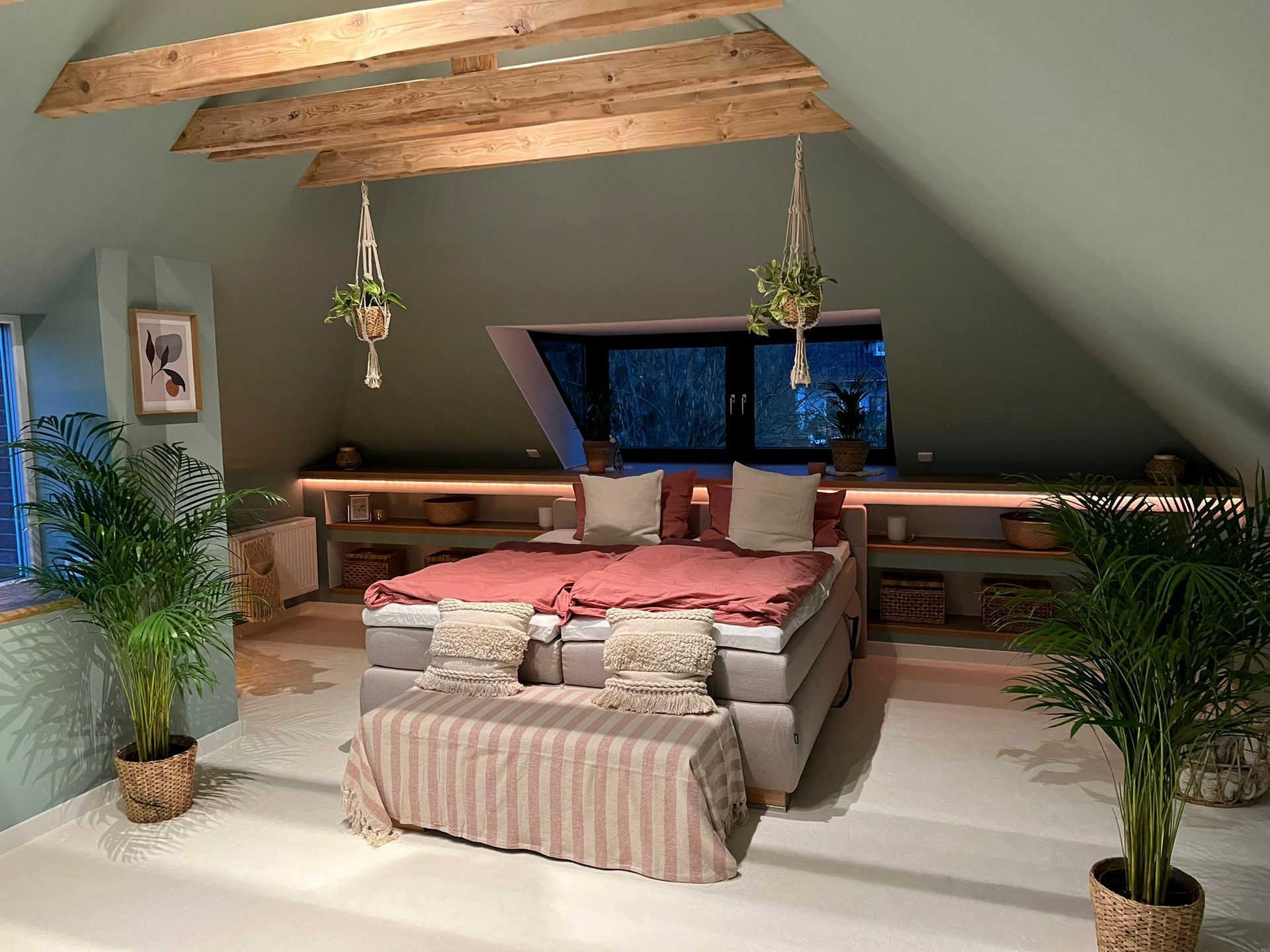 ein Schlafzimmer mit Bett, Bank, Pflanzen und Fenster.