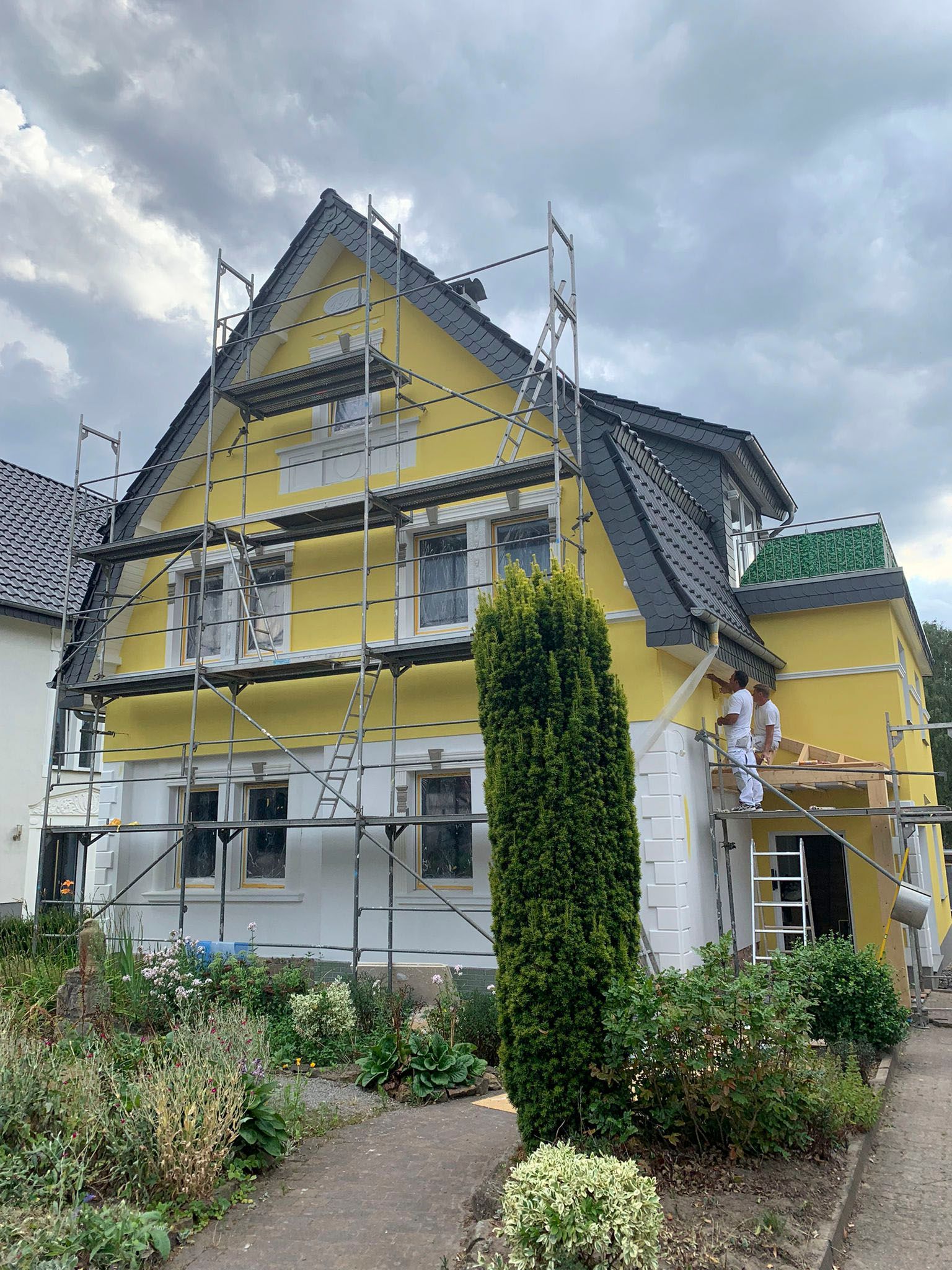 Es wird ein gelbes Haus gestrichen, das von einem Gerüst umgeben ist.