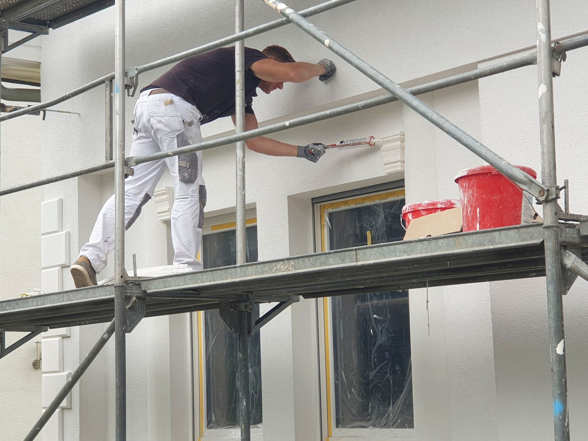 Ein Mann malt auf einem Gerüst die Seite eines Gebäudes.