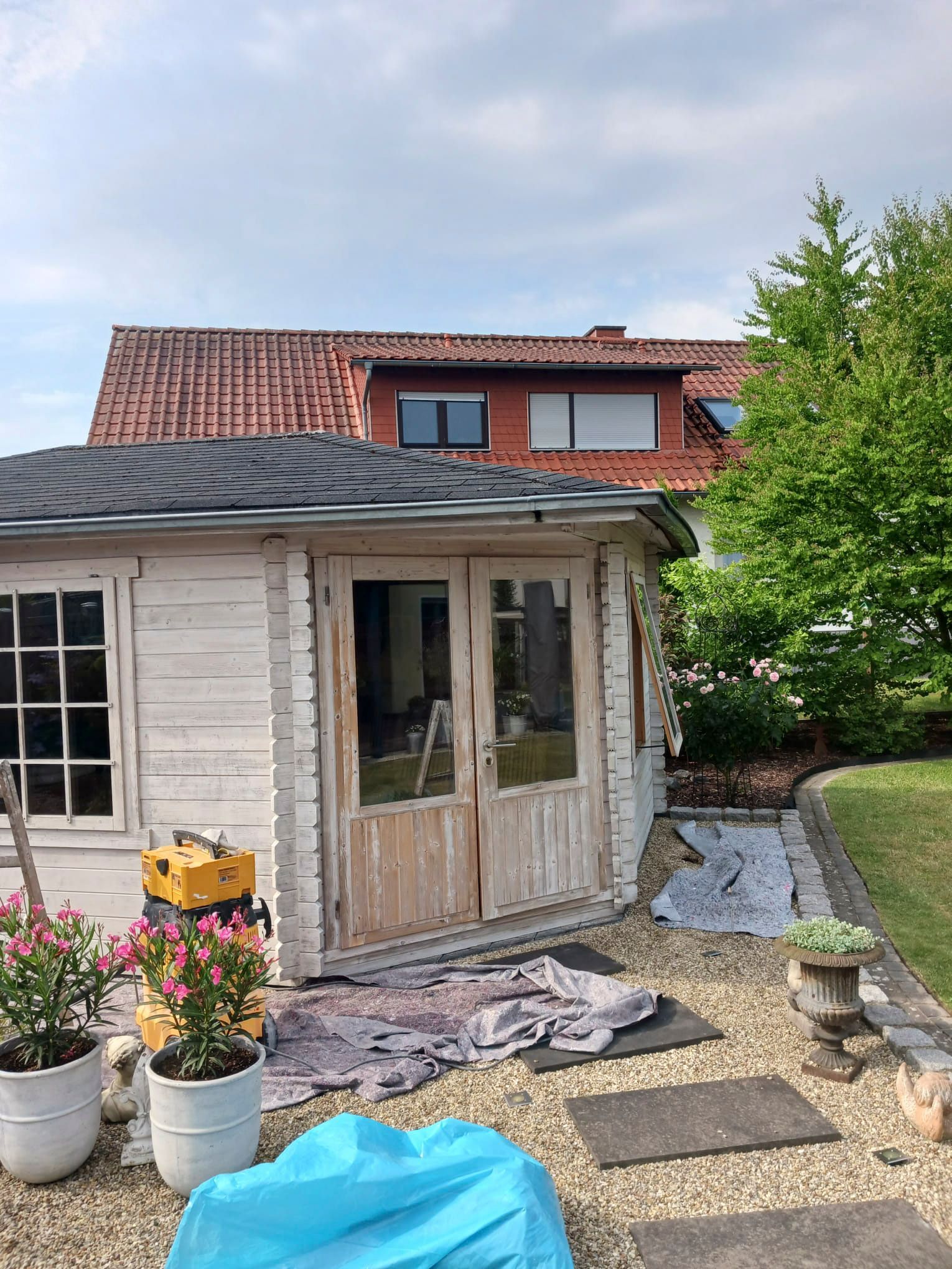 In einem Hinterhof wird ein weißes Holzhaus gestrichen.