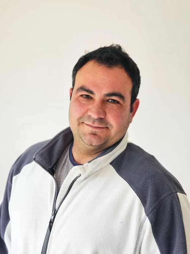 Ein Mann in einer weiß-grauen Jacke lächelt in die Kamera.