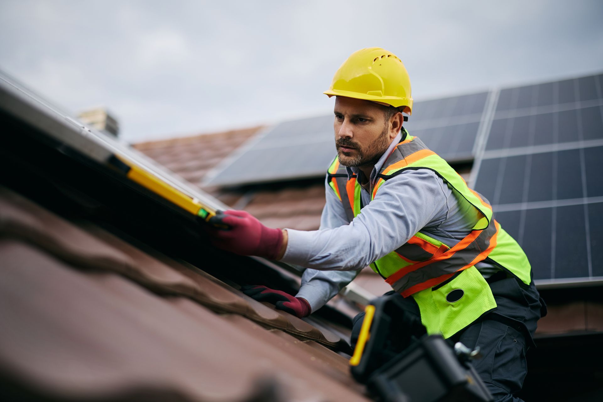 Installateur de panneaux solaires sur un toit, portant un casque jaune et un gilet de sécurité, travaillant sur les panneaux.