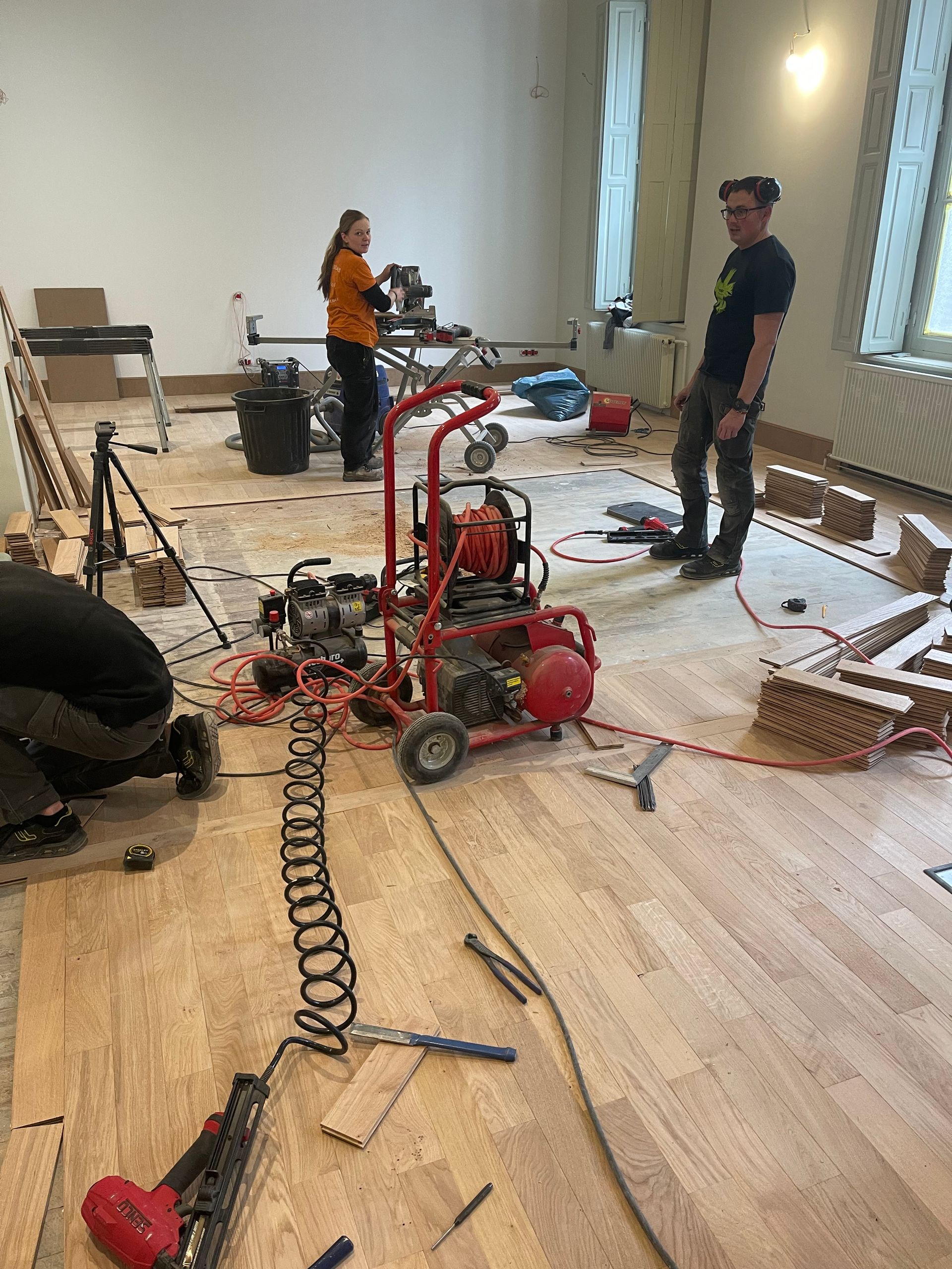 Des personnes installent un parquet en bois dur avec des outils dans une pièce.