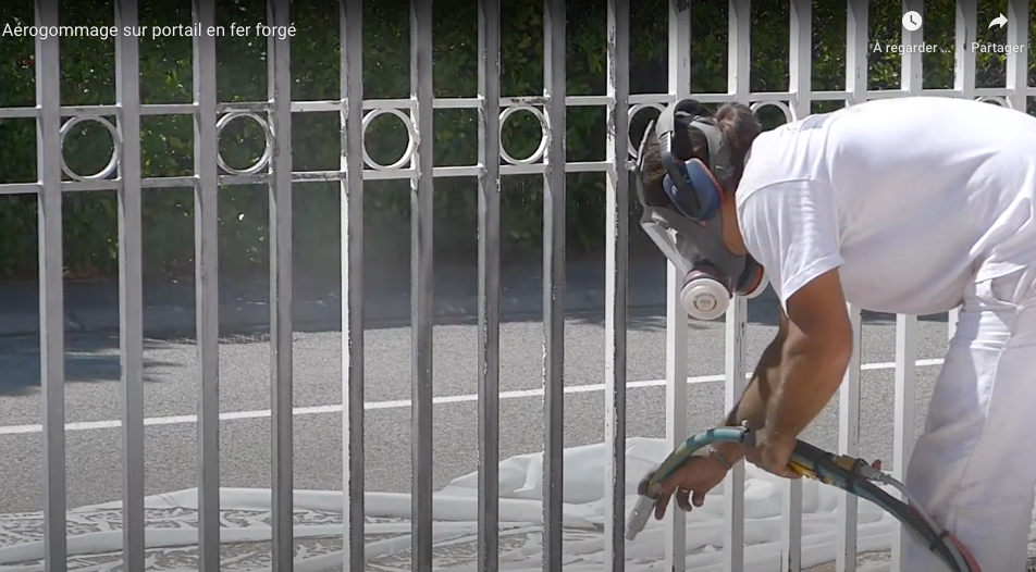 Technicien enlevant la peinture blanche d'un portail grâce à l'aérogommage