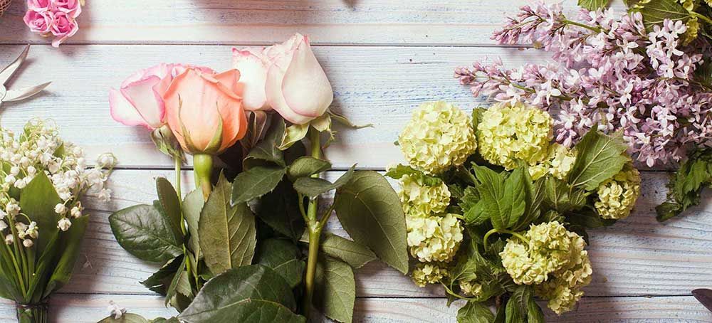 Variedad de flores en tonos pastel dispuestas sobre una superficie de madera blanca.