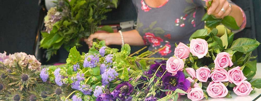 Persona arreglando rosas rosadas y flores moradas en una floristería.