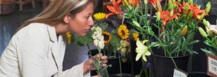 Una mujer huele flores en un puesto de mercado con coloridos ramos y plantas en macetas.