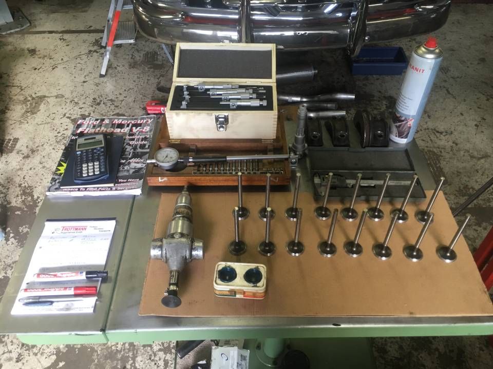 Werkstatttisch mit Motorteilen, Werkzeugen und einem Teilekatalog.