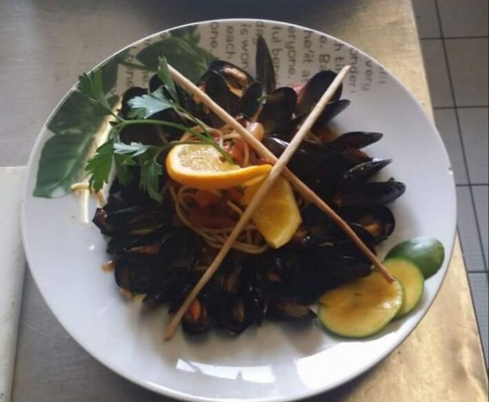 Teller mit Miesmuscheln, Nudeln, Zitronenscheiben, Petersilie und Grissini.