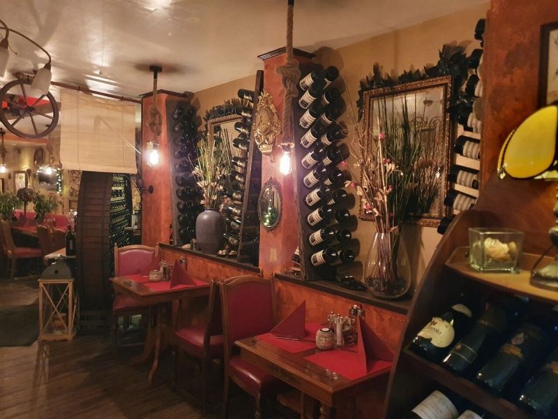 Restaurantinterieur mit roten Tischen, Weinregalen und Zierpflanzen.