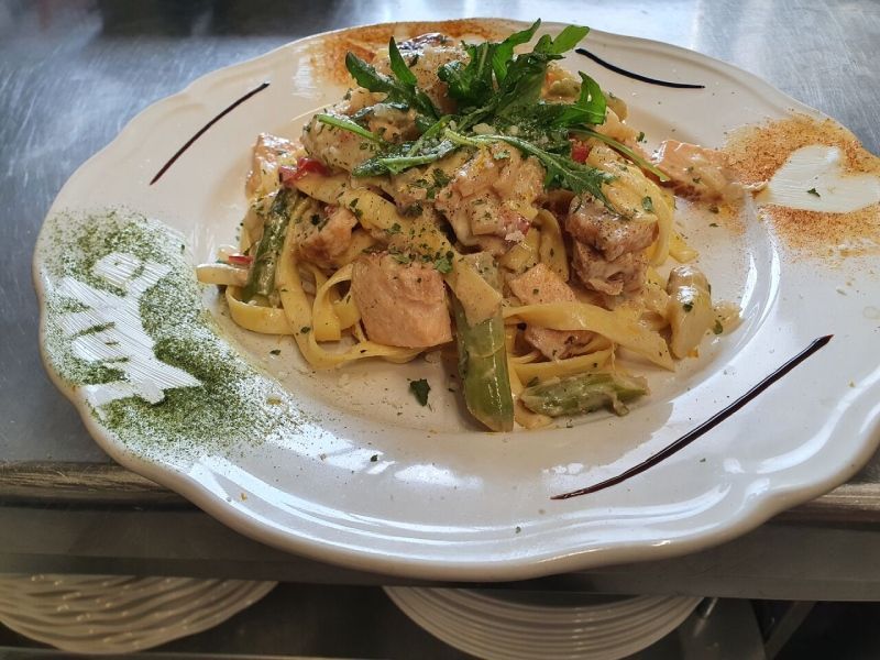 Pastagericht mit Lachs, Spargel und Kräutern auf einem dekorativen Teller.