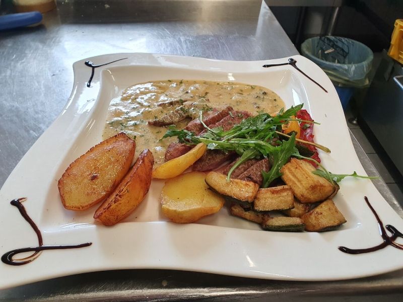 Steakteller mit cremiger Soße, Bratkartoffeln, gegrilltem Gemüse und Rucola.