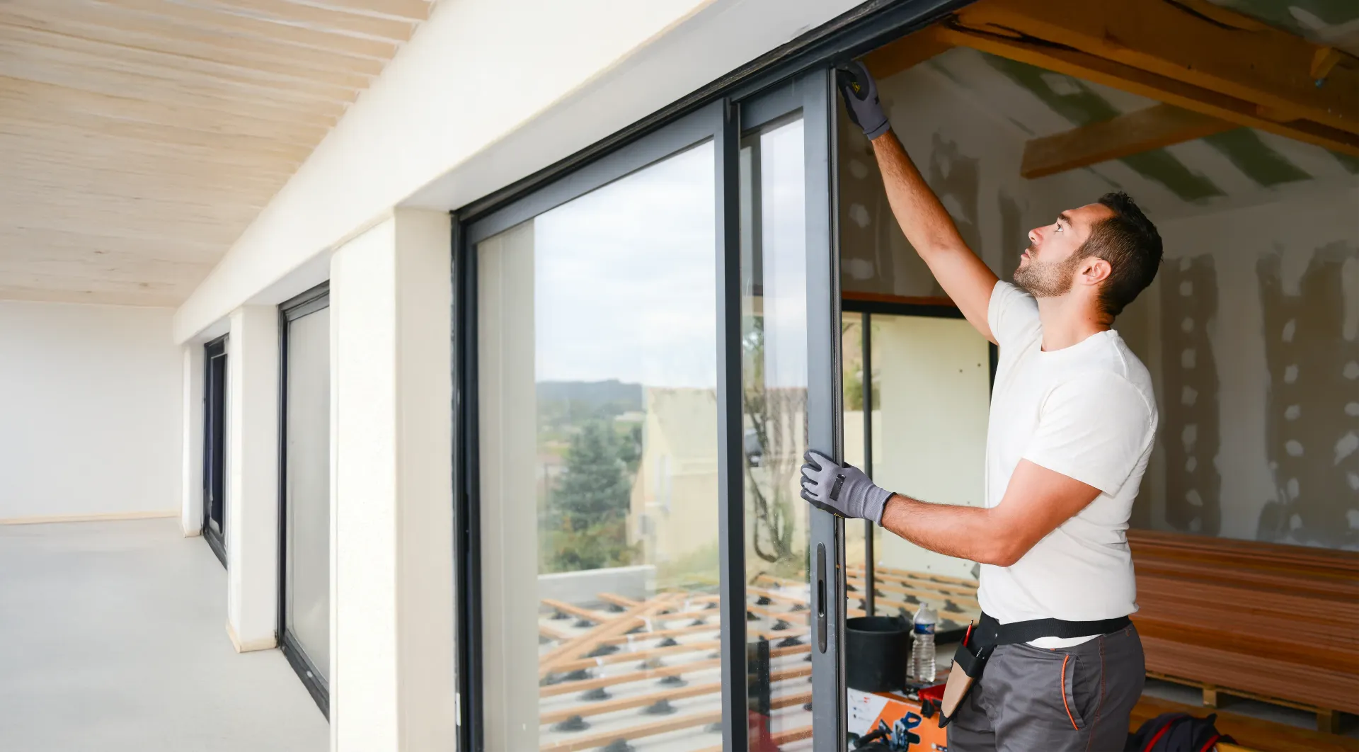 Hombre instalando una puerta corrediza de vidrio en exteriores. Se ven los materiales de construcción y el interior parcialmente terminado.