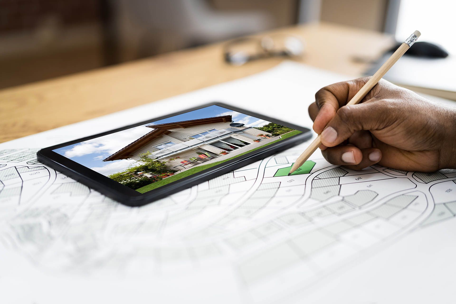 Eine Person markiert mit einem Bleistift eine Karte, während sie ein Haus auf einem Tablet betrachtet.