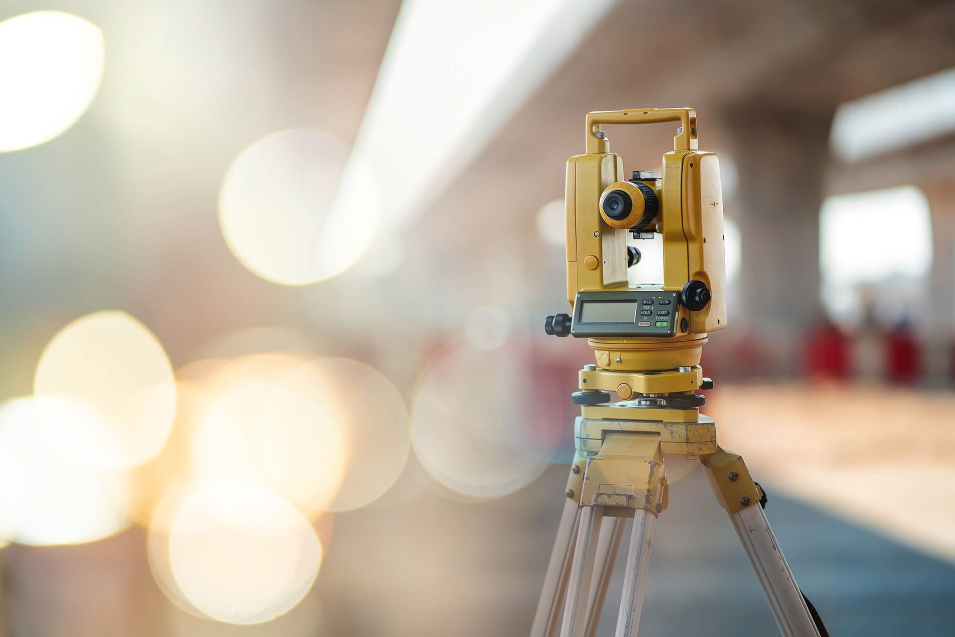 Gelber Theodolit auf Stativ, Messung im Baustellenumfeld.