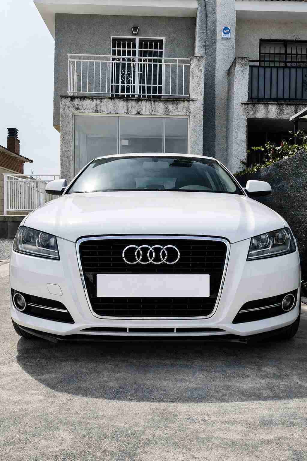 Sedán Audi blanco estacionado frente a un edificio residencial.