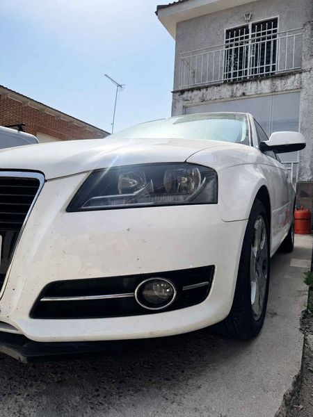 Sedán blanco estacionado en una entrada inclinada junto a una casa, vista frontal.