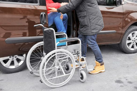 Person hilft einer Person im Rollstuhl aus einem Auto heraus
