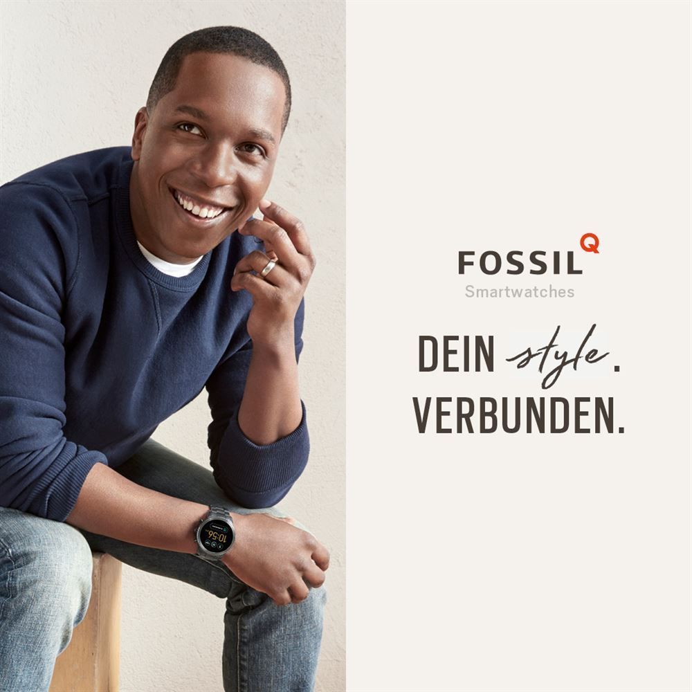 Ein Mann sitzt auf einem Hocker und trägt eine Smartwatch von Fossil.