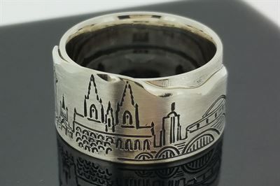 Ein silberner Ring mit der Skyline einer Stadt liegt auf einer schwarzen Oberfläche.