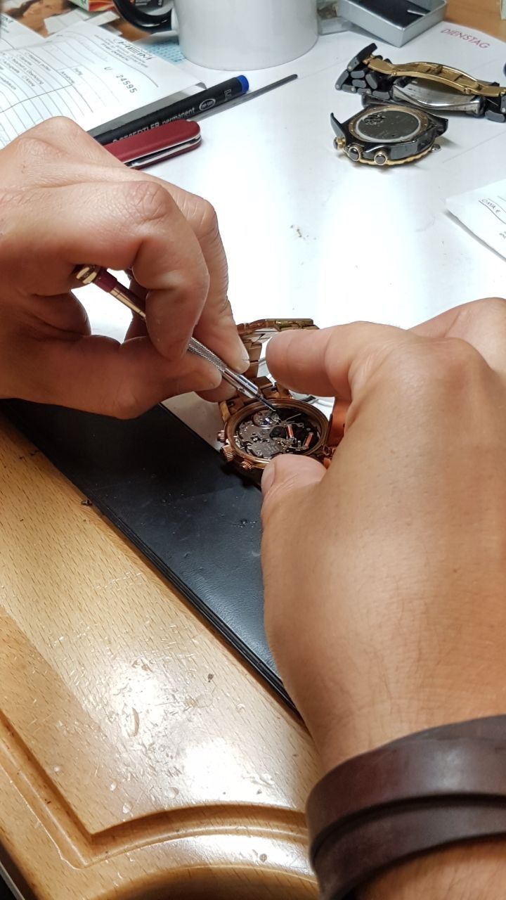 Eine Person bearbeitet mit einer Pinzette eine Uhr.