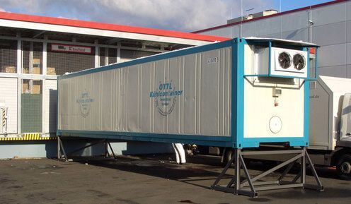 Ein blau-weißer Kühlcontainer von OTTL-CONTAINER steht vor einem Gebäude