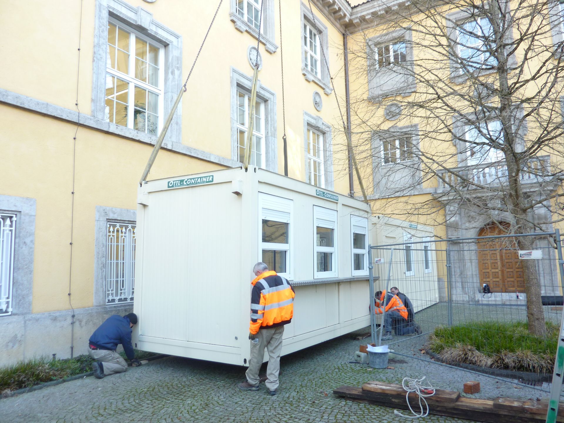 Ein Bürocontainer wird mit einem Kran vor einem Gebäude platziert