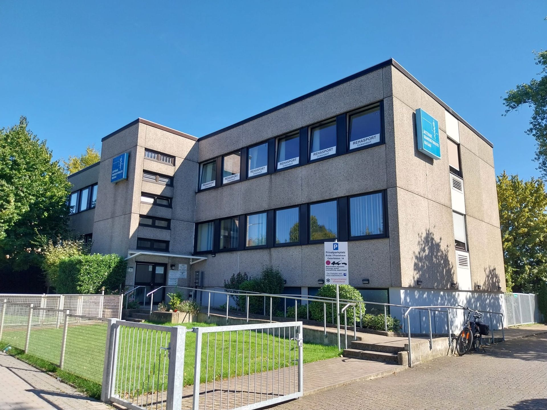 Modernes dreistöckiges Bürogebäude mit großen Fenstern, umgeben von einer umzäunten Rasenfläche an einem sonnigen Tag