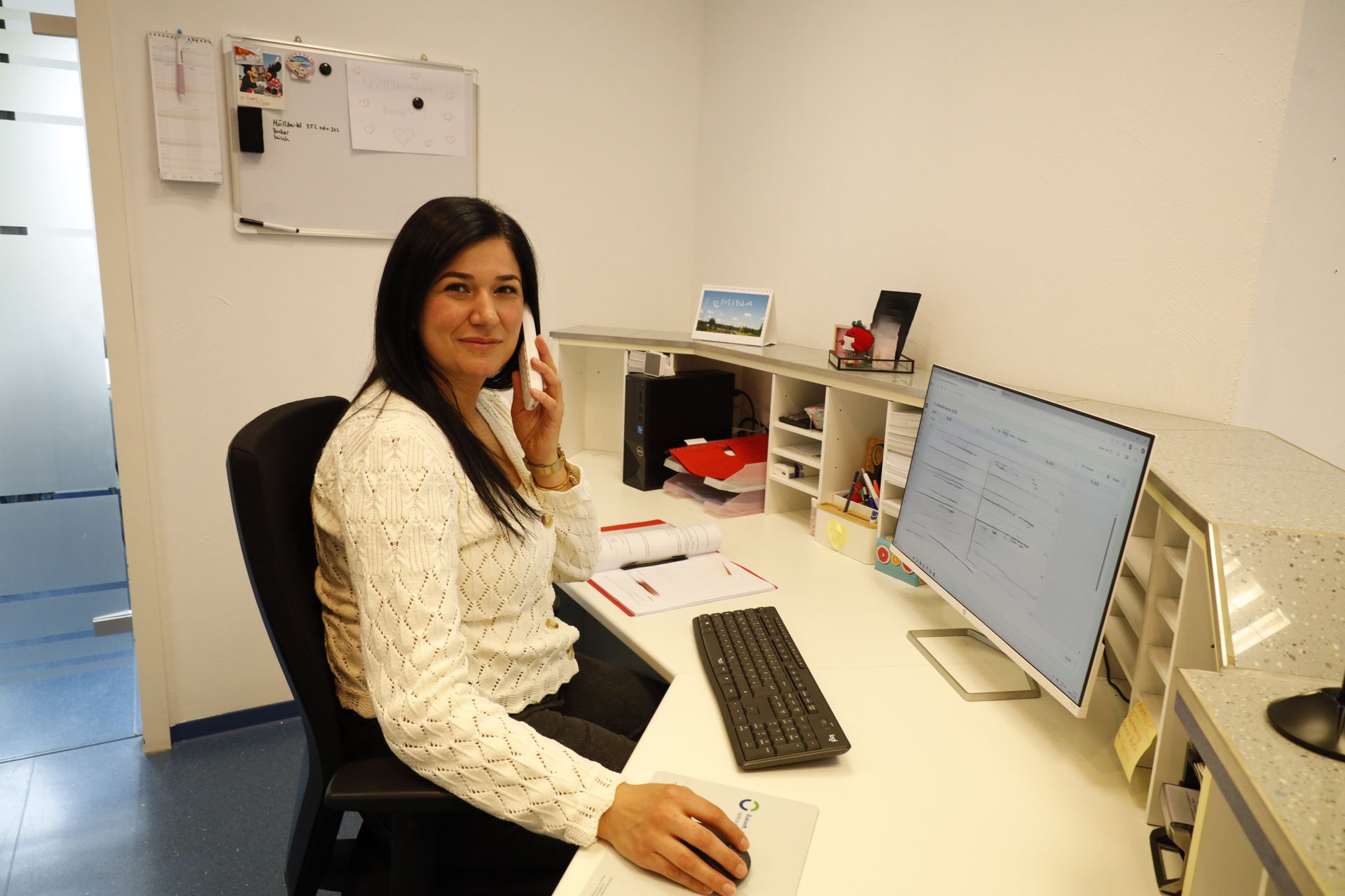 Frau an einem Schreibtisch in einem Büro, lächelt und telefoniert. 