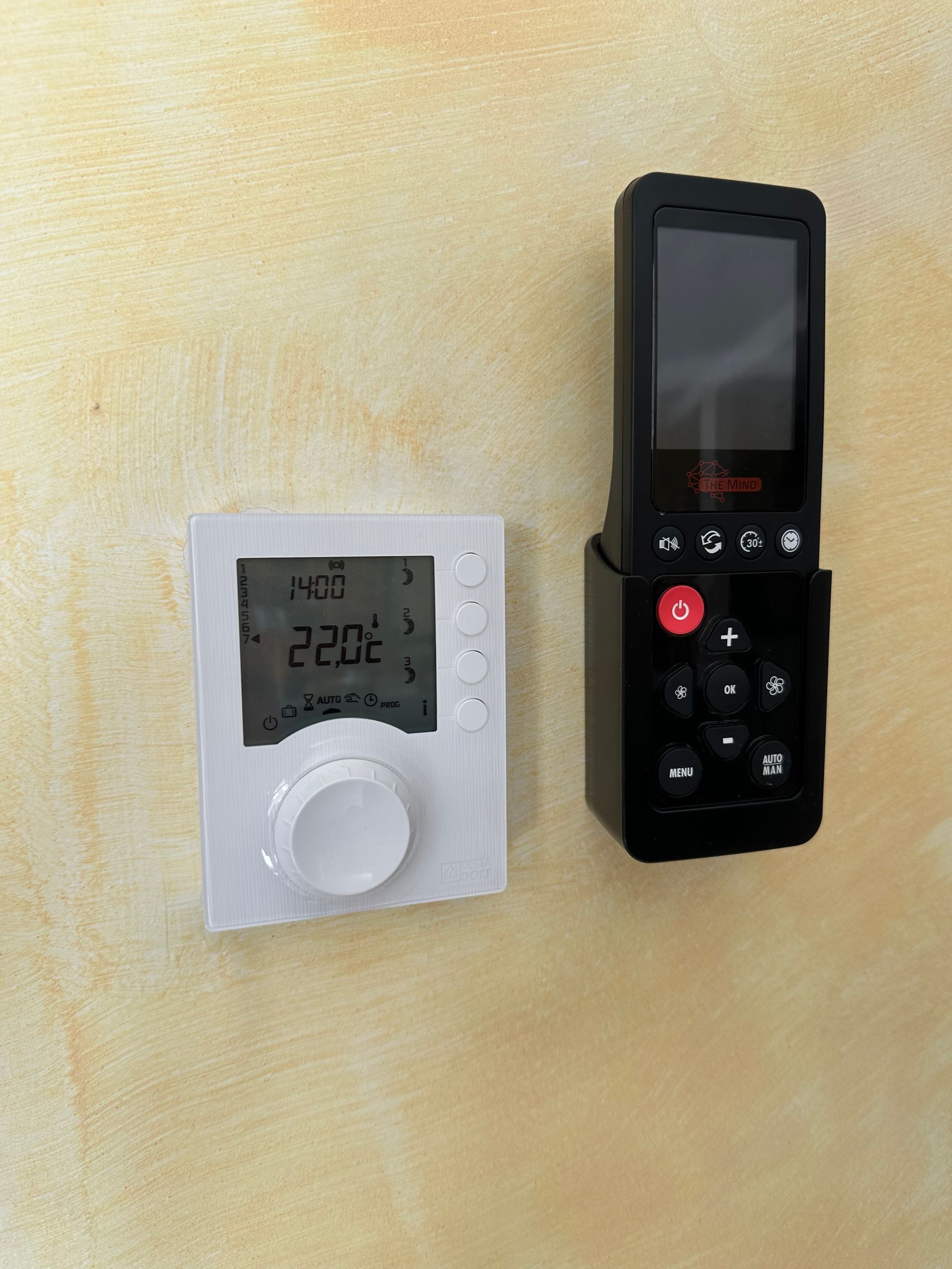 Thermostat blanc et télécommande noire fixés sur un mur clair.