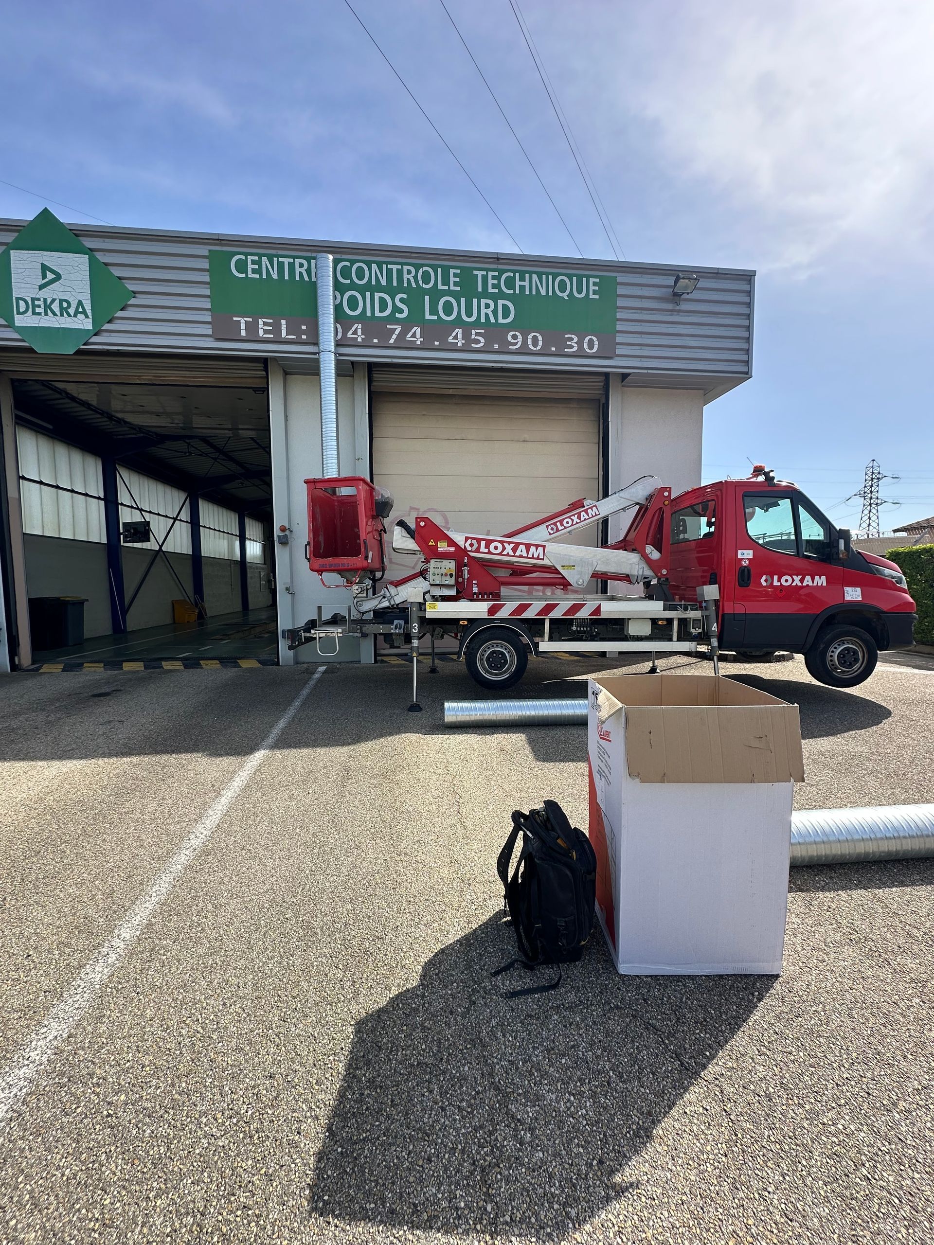 Camion rouge équipé d'une nacelle élévatrice stationné devant un bâtiment avec un panneau vert.