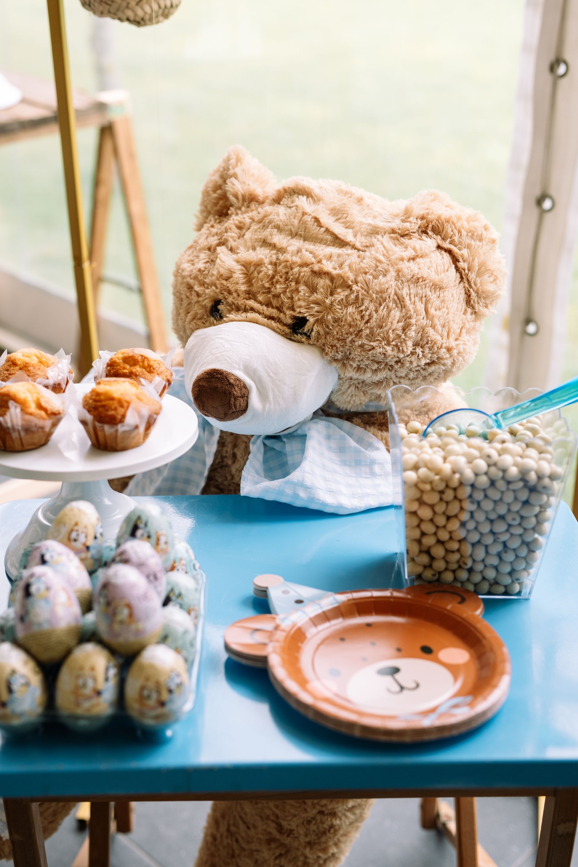 Un osito de peluche está sentado en una mesa con platos y huevos.