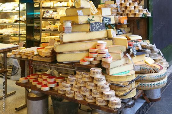 Des fromages et des produits laitiers empilés sont présentés dans un magasin, avec des étagères et des paniers remplis de meules et de portions.