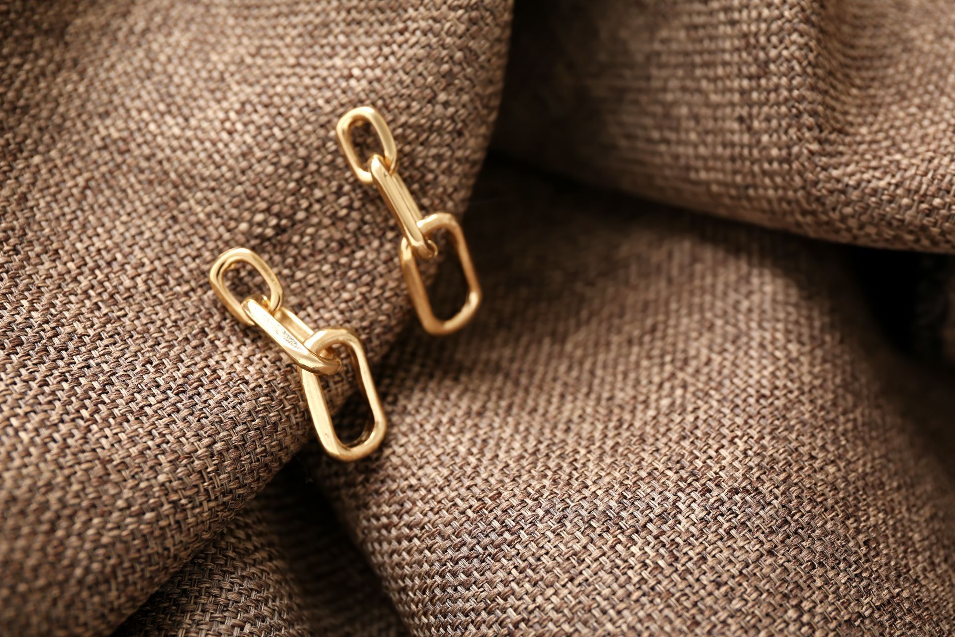 Boutons de manchette en or sur un tissu gris texturé.