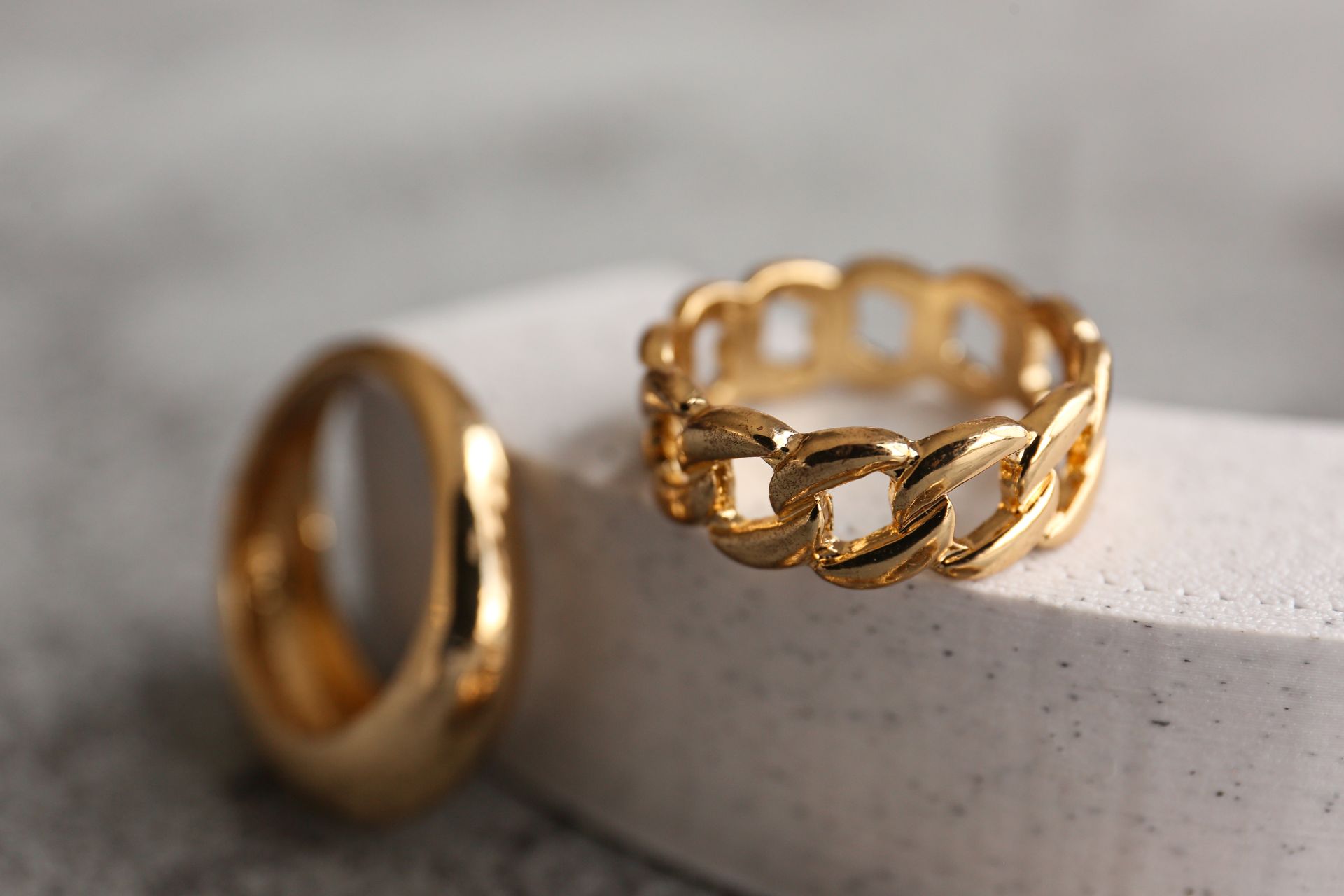 Deux anneaux en or, l'un lisse, l'autre de type maillon de chaîne, sur une surface blanche texturée.