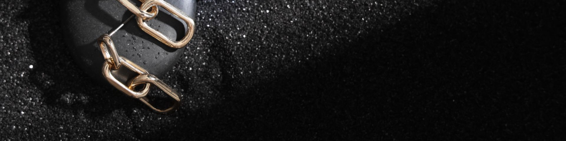 Boucles d'oreilles en chaîne dorée sur une surface texturée noire, avec une ombre.