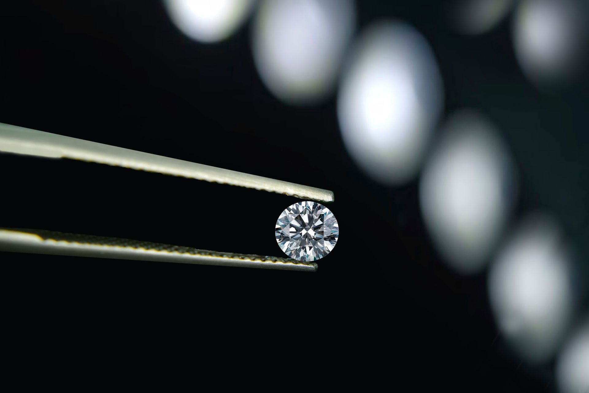 Diamant tenu par une pince à épiler sur un fond sombre avec des lumières floues.