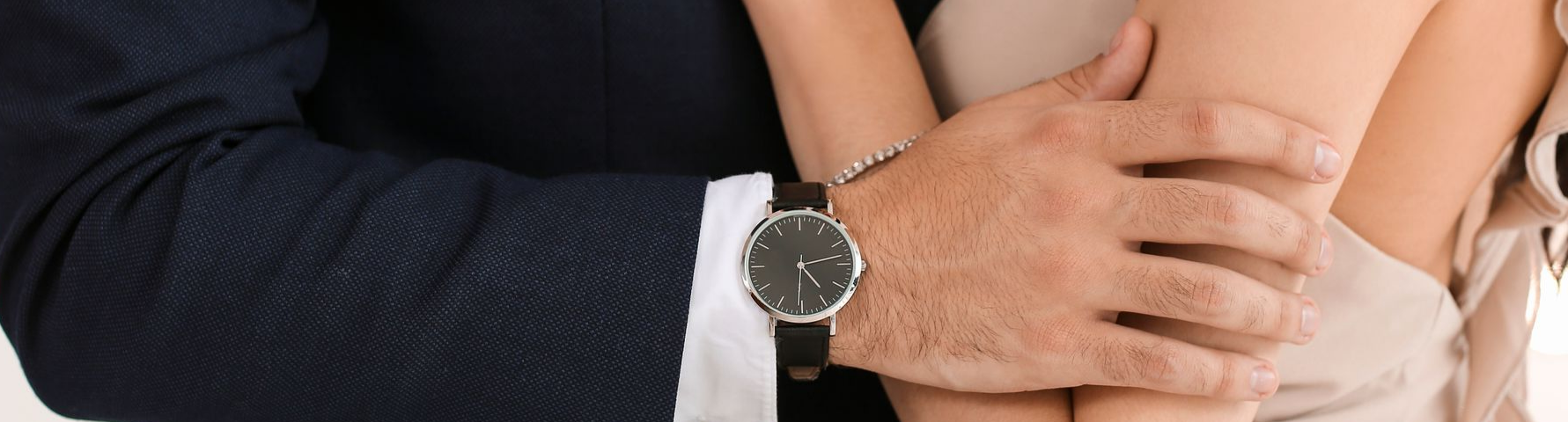 La main d'un homme tient doucement le bras d'une femme. Il porte une montre et un costume bleu.