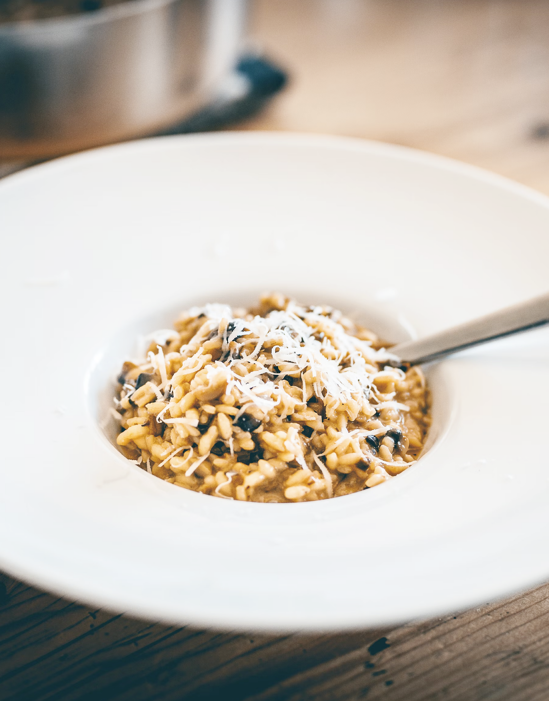 Risotto en un recipiente blanco, cubierto con queso, sobre una mesa de madera.