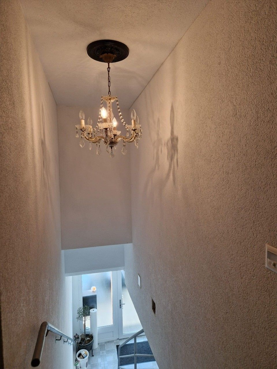 Von der Decke eines Treppenhauses hängt ein Kronleuchter.