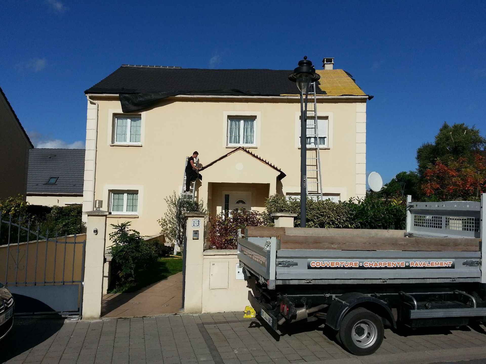 Une maison avec un toit en rénovation et le camion de l'entreprise garé devant