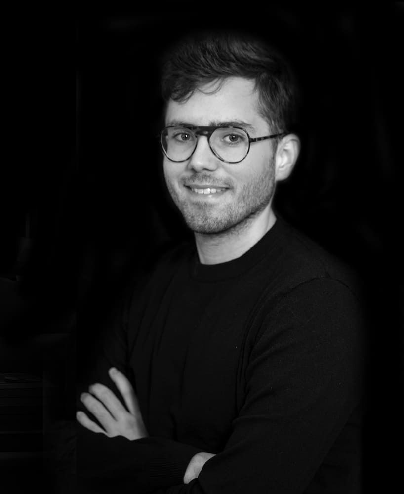 Una fotografía en blanco y negro de un hombre que lleva gafas y un suéter negro.