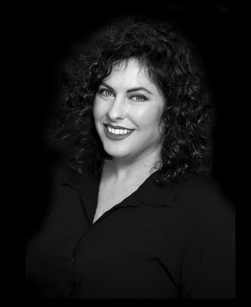 Una mujer con cabello rizado sonríe en una foto en blanco y negro.