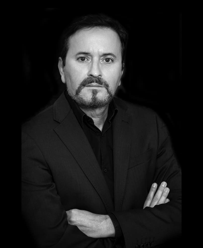 Una fotografía en blanco y negro de un hombre con traje y los brazos cruzados.