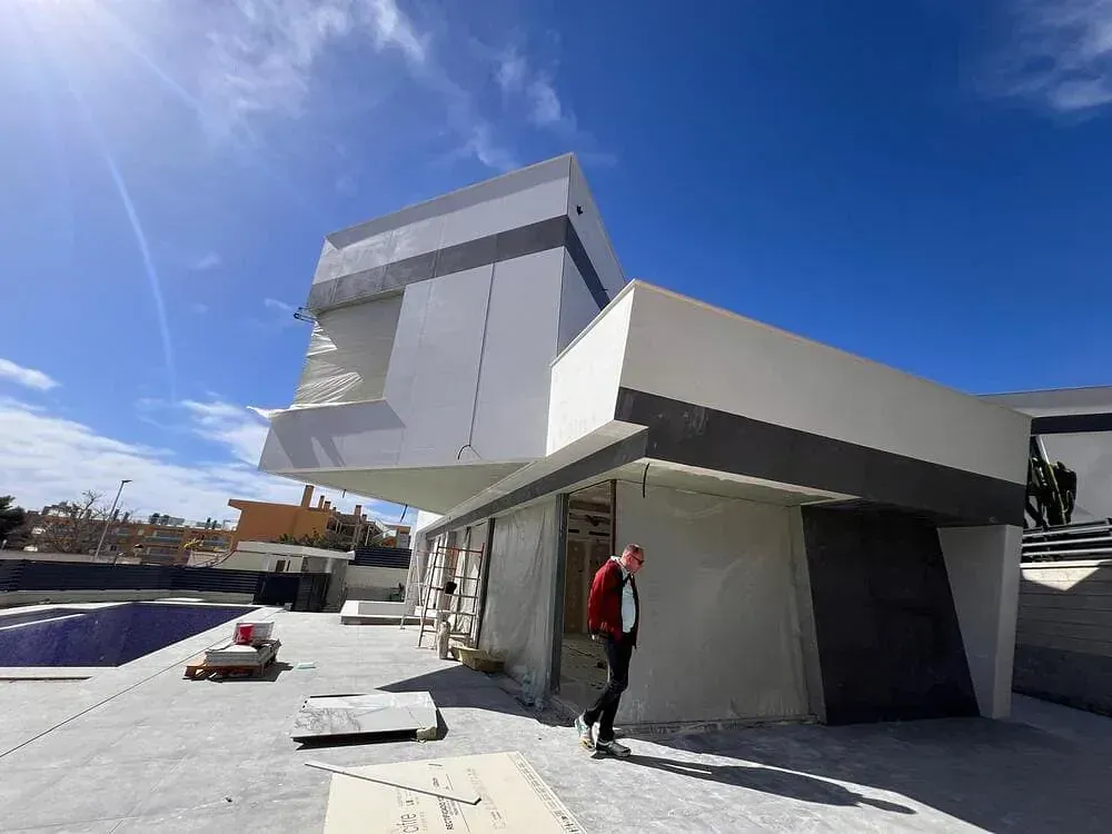Un hombre con un sombrero rojo camina frente a un edificio en construcción.