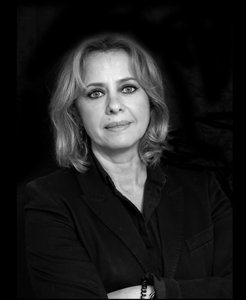 Una fotografía en blanco y negro de una mujer con traje y los brazos cruzados.