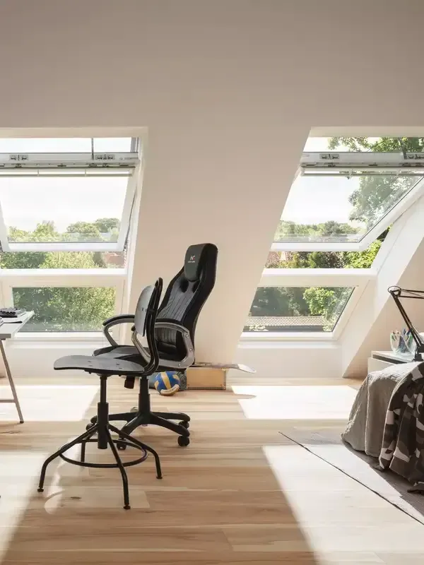 Ein Schlafzimmer mit Schreibtisch, Stuhl und vielen Dachfenstern.
