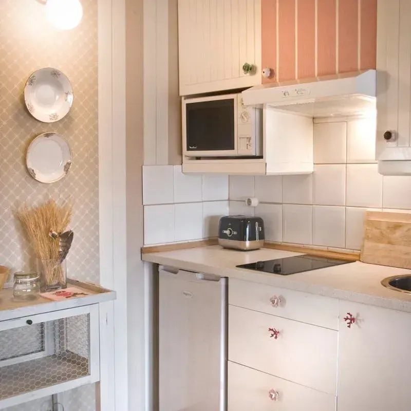 Pequeña cocina con gabinetes blancos, microondas y tostadora; decorada con platos y detalles en rosa.