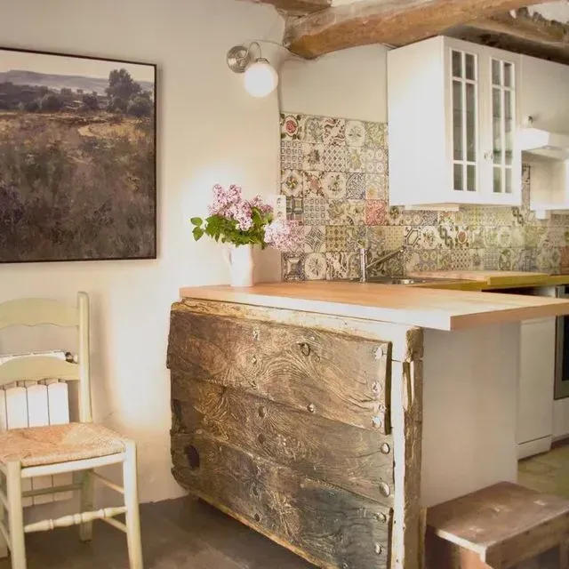 Acogedora cocina con frentes de gabinetes de madera y protector contra salpicaduras de azulejos florales; pintura en la pared.